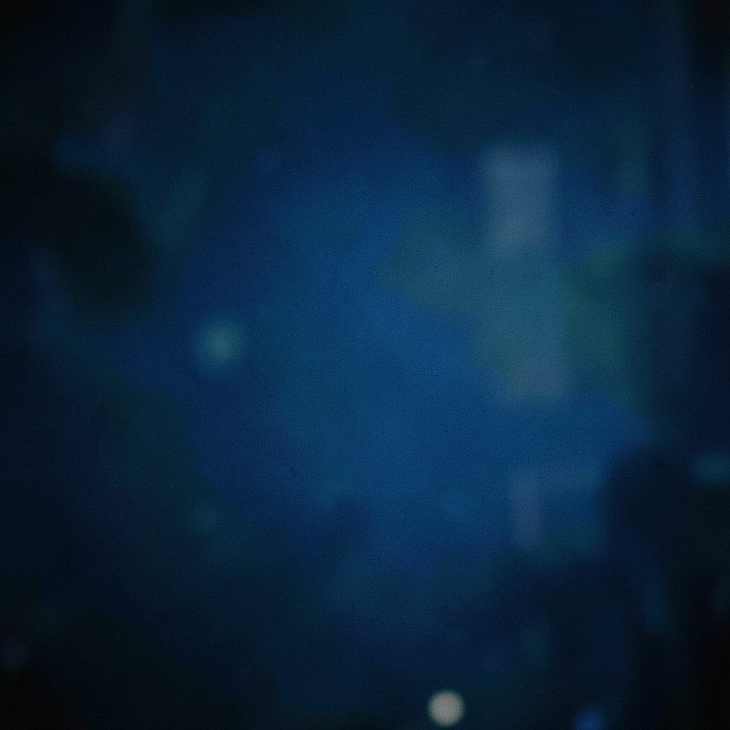 Wide cinematic frame of a softly lit conference room with a lone presenter at the front, warm amber and deep navy tones, shallow depth of field